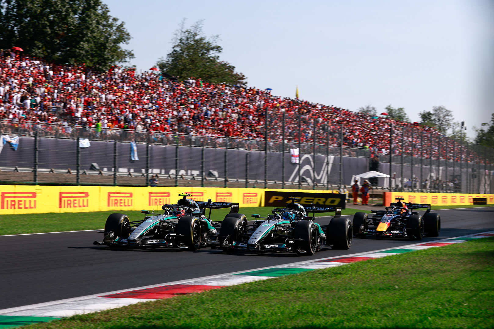 Delle vetture di Formula Uno sfrecciano in pista a Monza sotto la tribuna gremita.