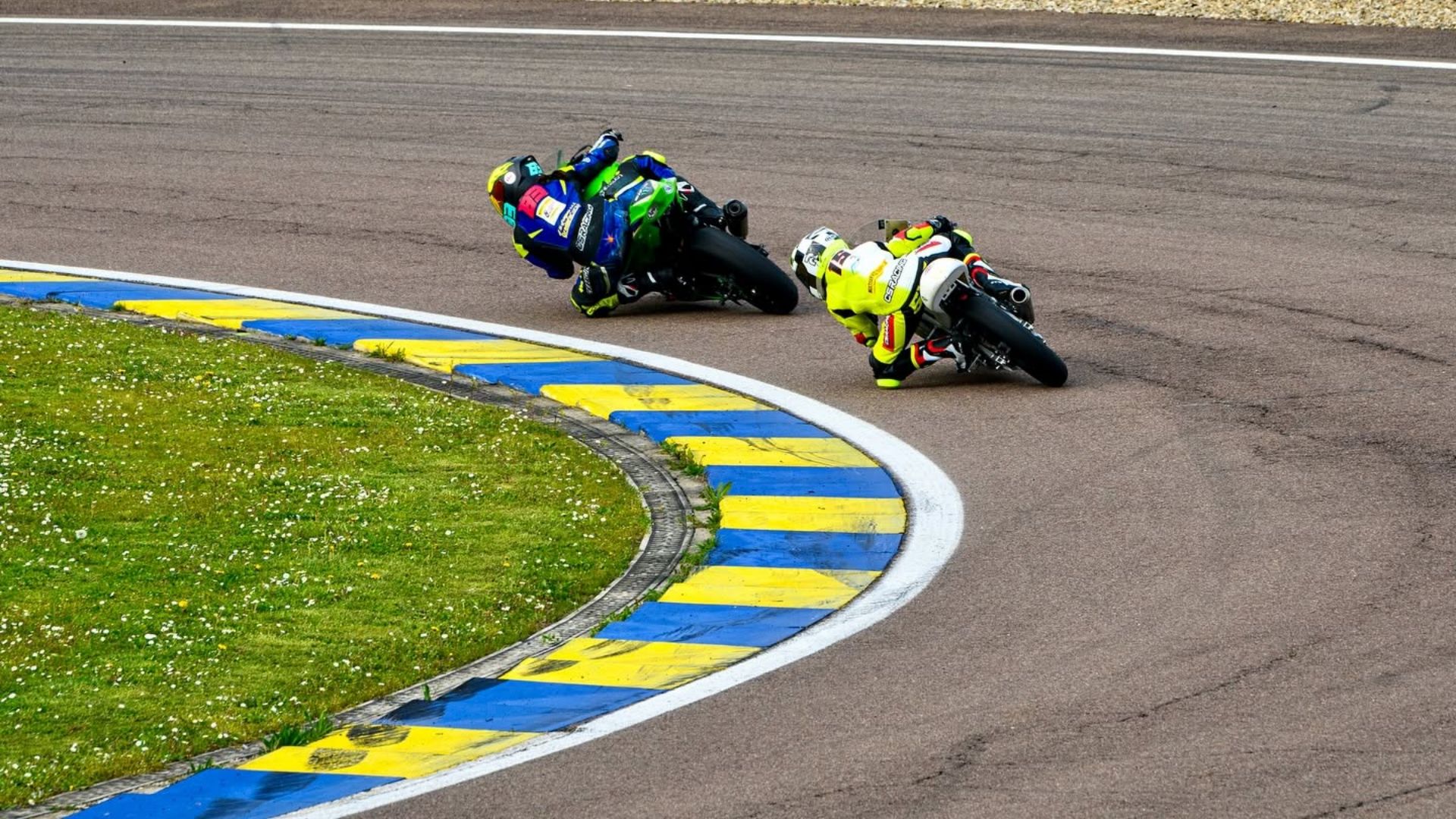 Gara di motociclismo su circuito asfaltato con due piloti che affrontano una curva a sinistra molto piegati, toccando il cordolo giallo e blu all'Autodromo di Modena durante i Track Days Luca Pedersoli.